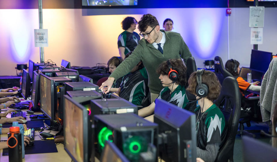 two students playing esports on a computer while an instructor looks on