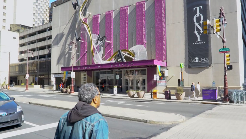 Modal Image Opens to lightbox video- Lindsay Smiling walking in front of the Tony award-winning Wilma Theater