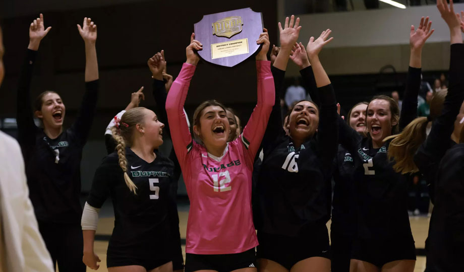 Volleyball players hoist trophy after win.