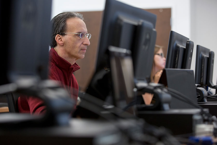 Man with glasses looking at row of computers.