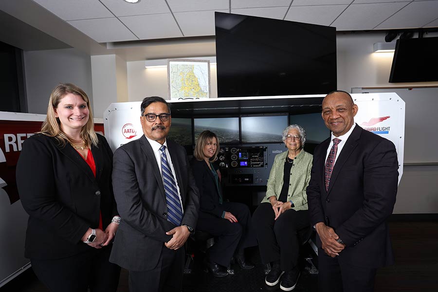 Five people stand in front of a Red Bird flight simulator.