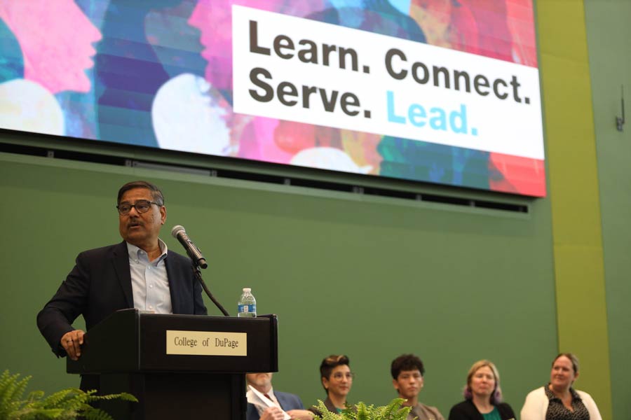 Dr. Muddassir Siddiqi speaking at a podium in front of a image on the screen that says learn, connect, serve and lead
