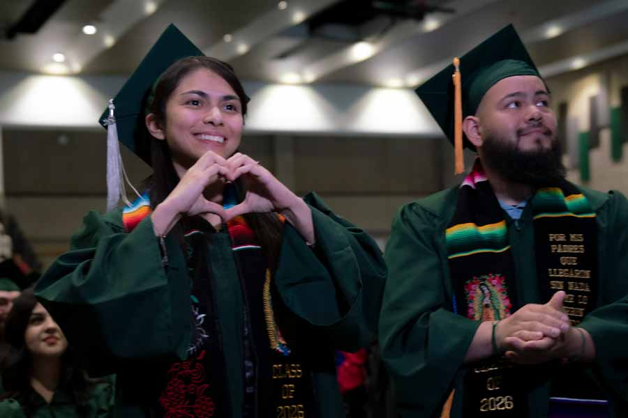 two graduates stand and smile while being recognized for academic achievement