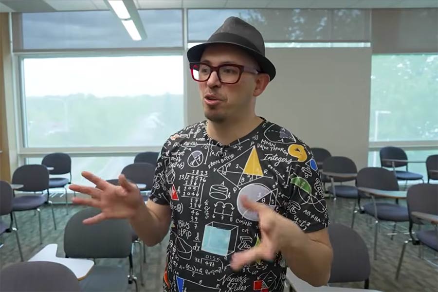 male faculty member wearing red glasses, a hat and a colorful shirt