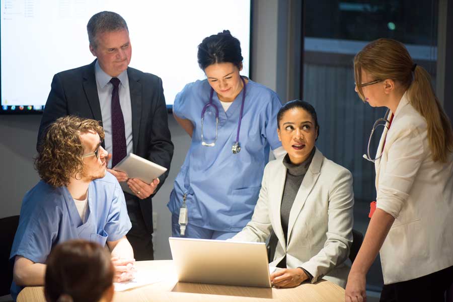 Healthcare professionals and administrators gather around a laptop during a team meeting.