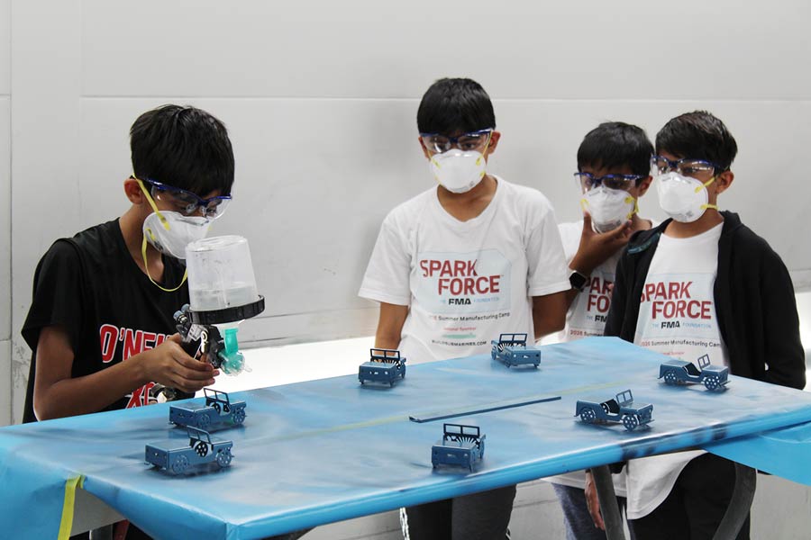 A young student liquid painting a model Jeep while three students watch.